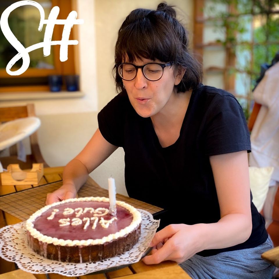 Dunkelhaarige Frau bläst Geburtstagskerze aus