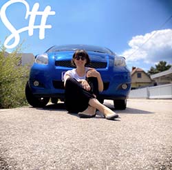 Frau sitzt am Boden vor blauem Auto und lächelt