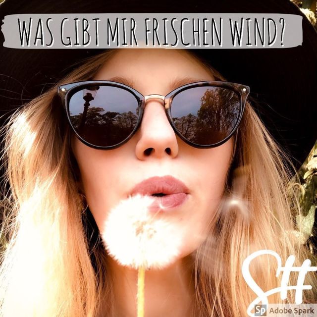 Frau mit Sonnenbrille und Hut bläst Löwenzahn