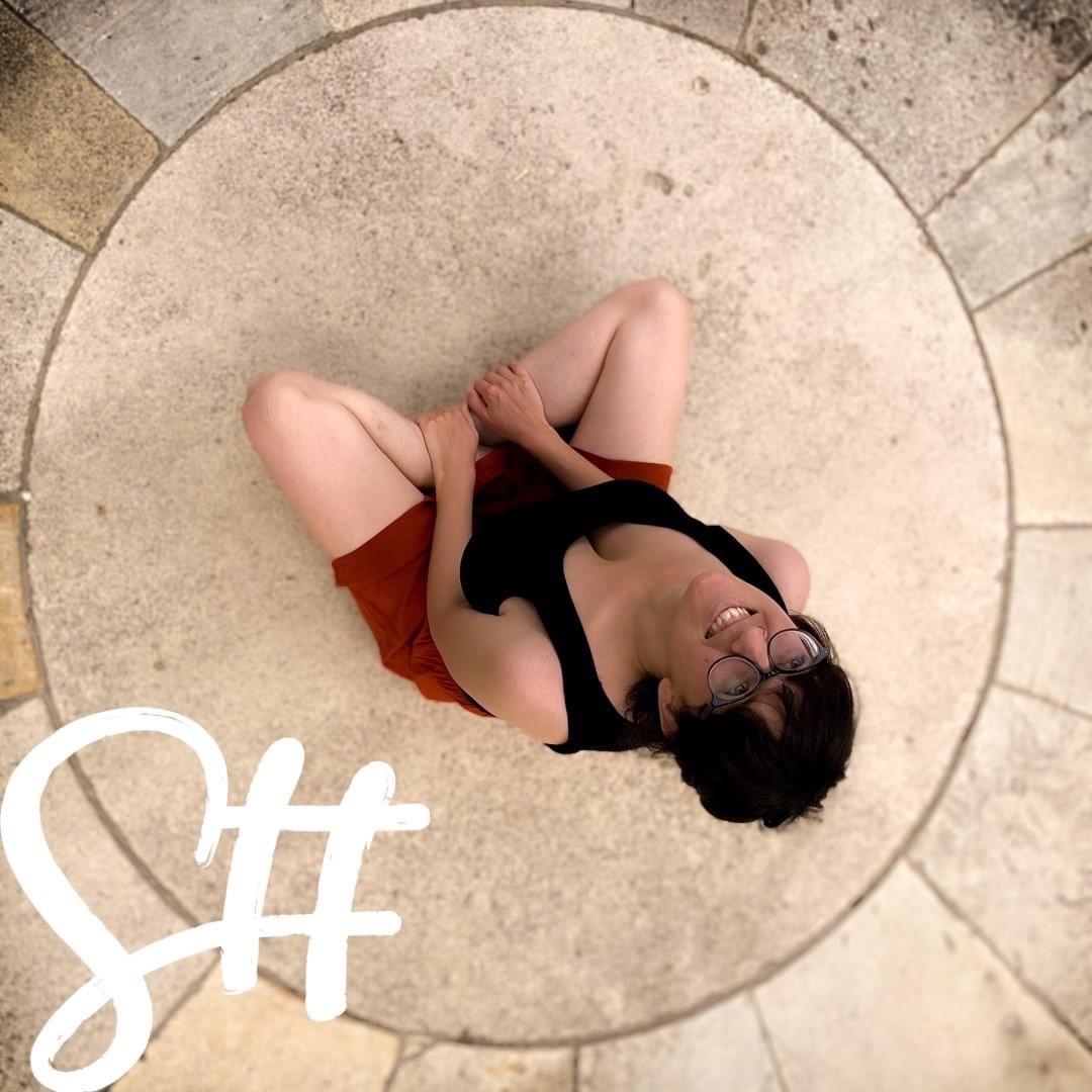 Dunkelhaarige Frau mit Brille sitzt am Steinboden und blickt in den Himmel