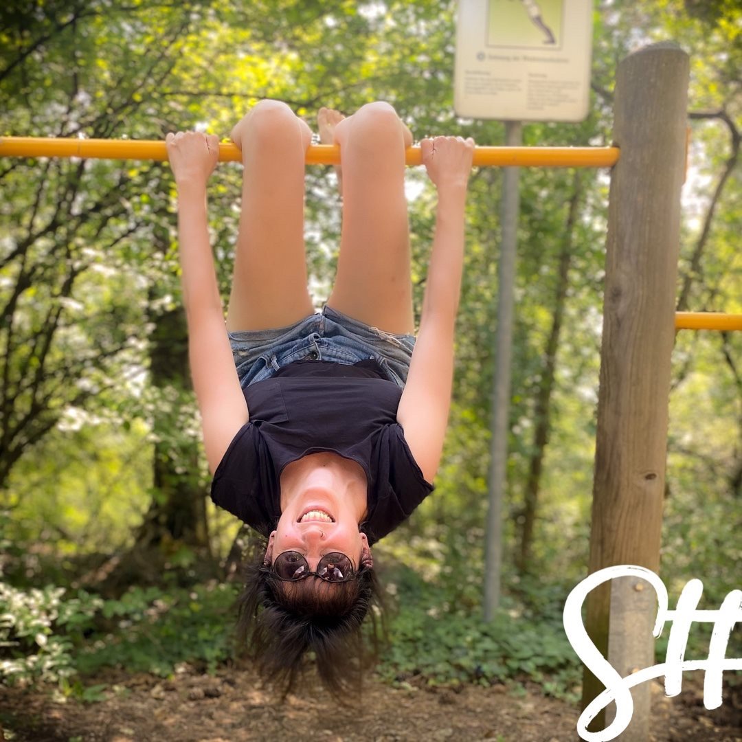 Frau hängt kopfüber auf einer Reckstange